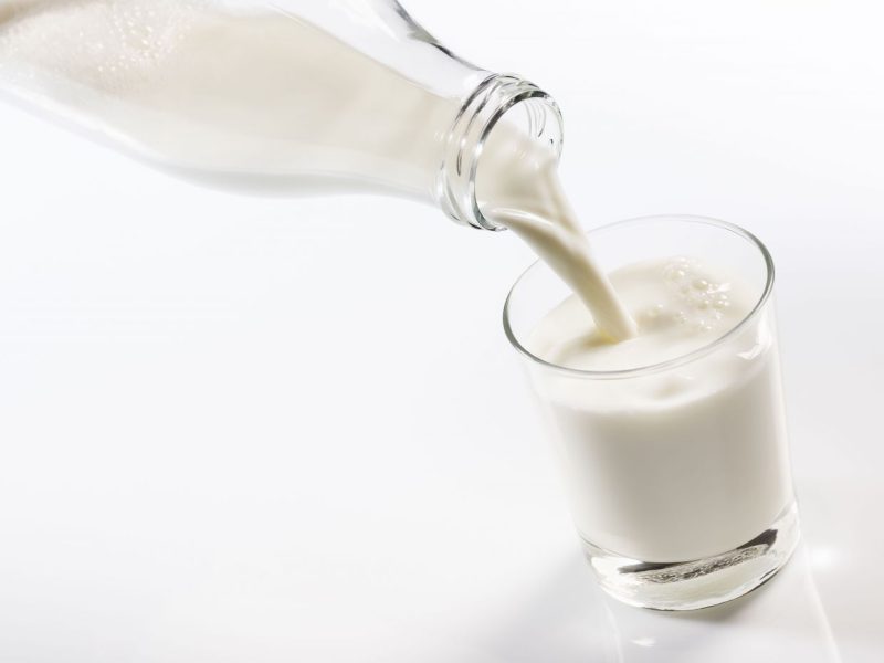 Milch wird aus der Milch-Glasflasche in ein Glas gelehrt