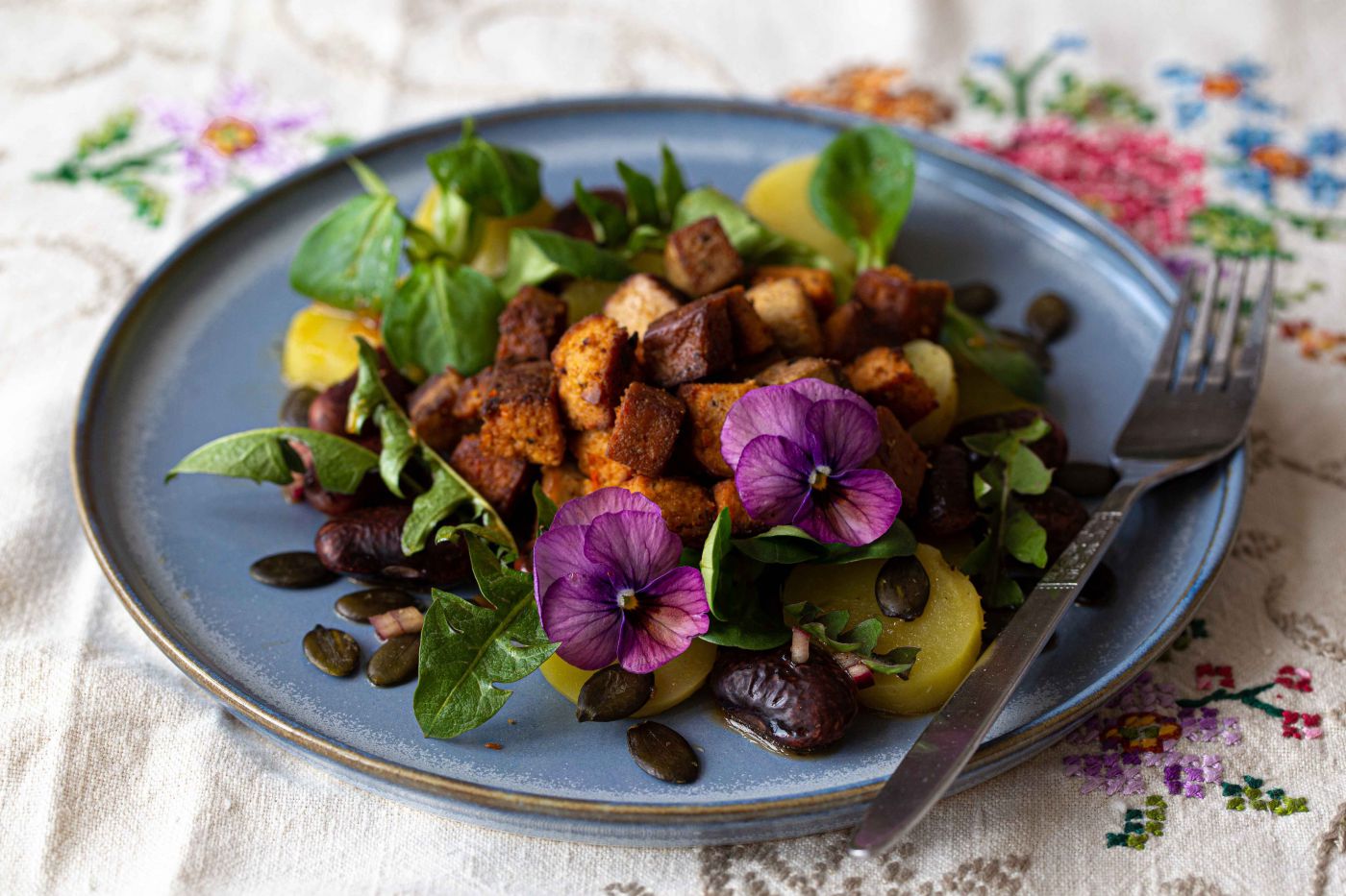 Löwenzahnsalat mit Tofu und Käferbohnen serviert am blauen Teller