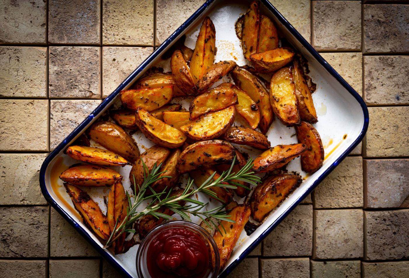 Potato Wedges in einer Auflaufform mit Rosmarin und Ketchup