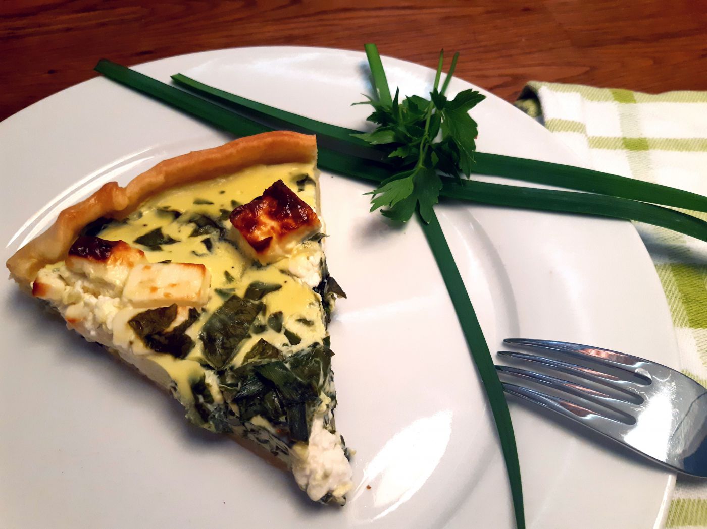 Ein Stück Spinat-Feta Quiche auf Teller mit Schnittlauch und Petersilie als Zierde