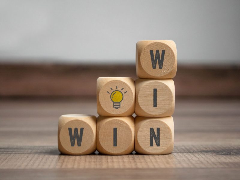 Holzwürfel mit den Buchstaben WinWin darauf und Glühbirne